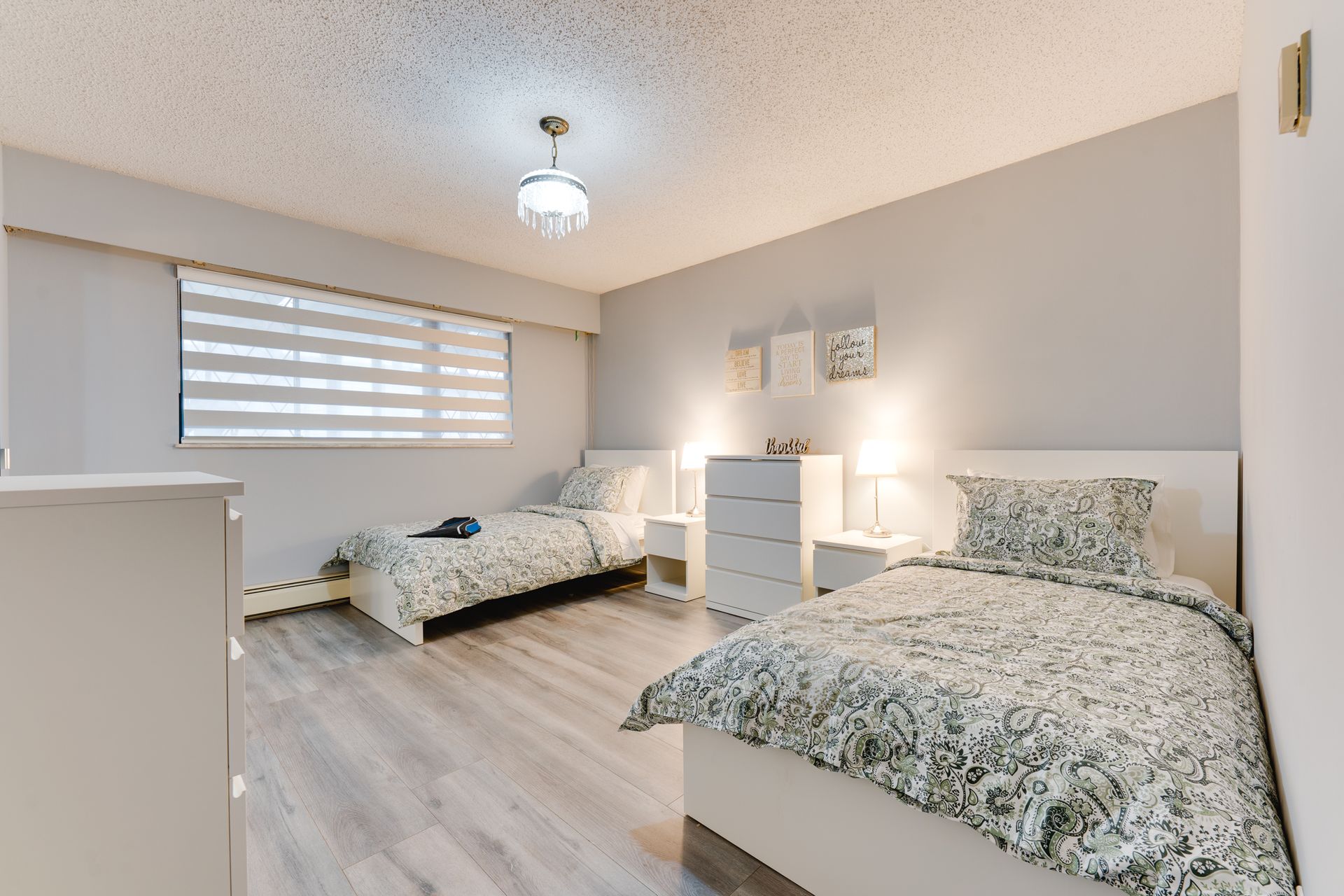 A bedroom with two beds , a dresser and a window.