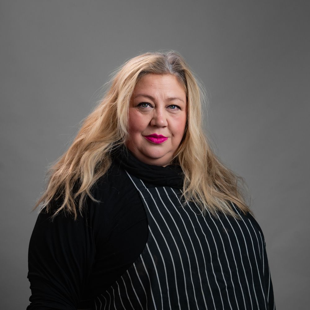 Woman with long blonde hair, wearing a black and white striped top, looking at the camera.