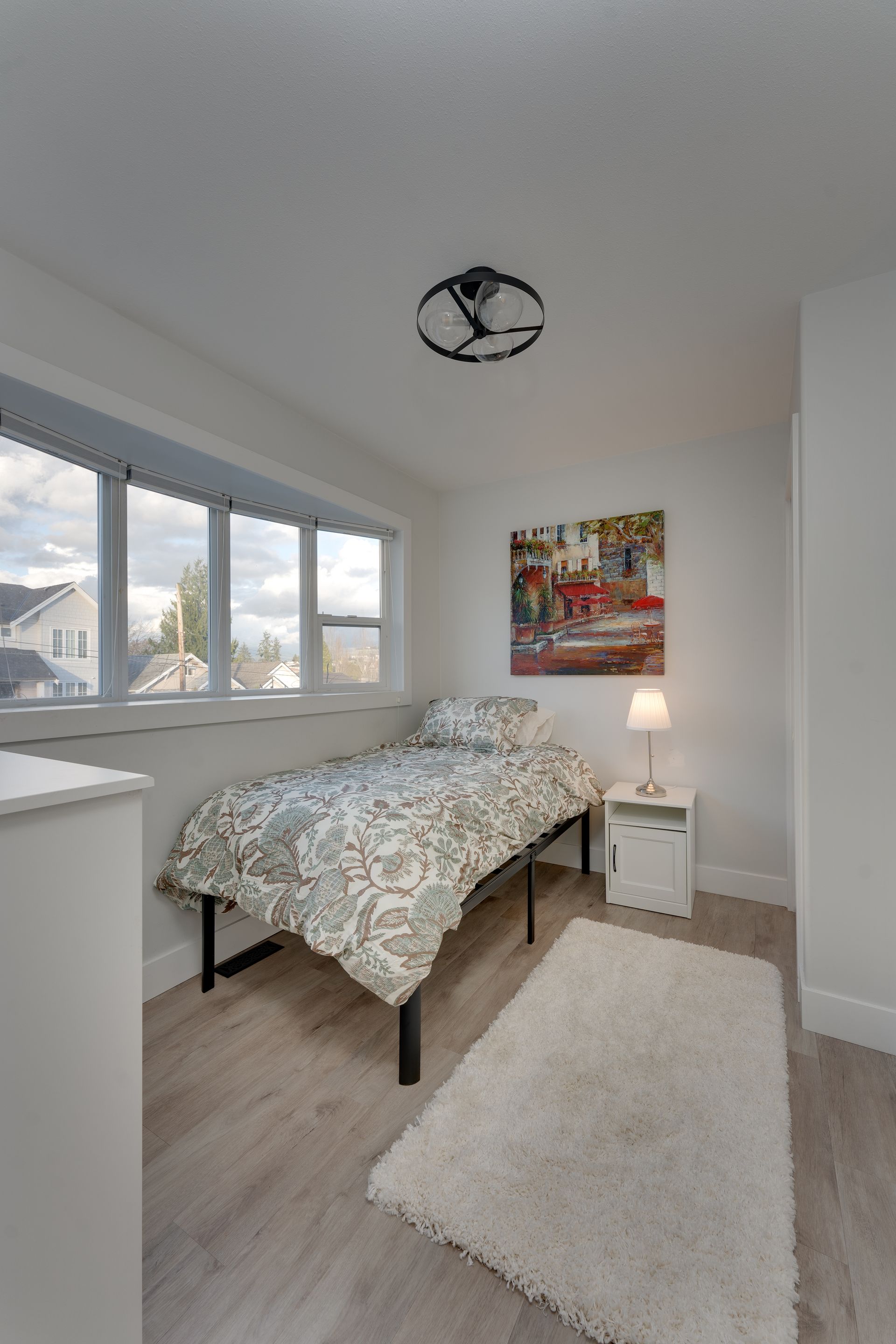 A bedroom with a bed , nightstand , rug and a painting on the wall.
