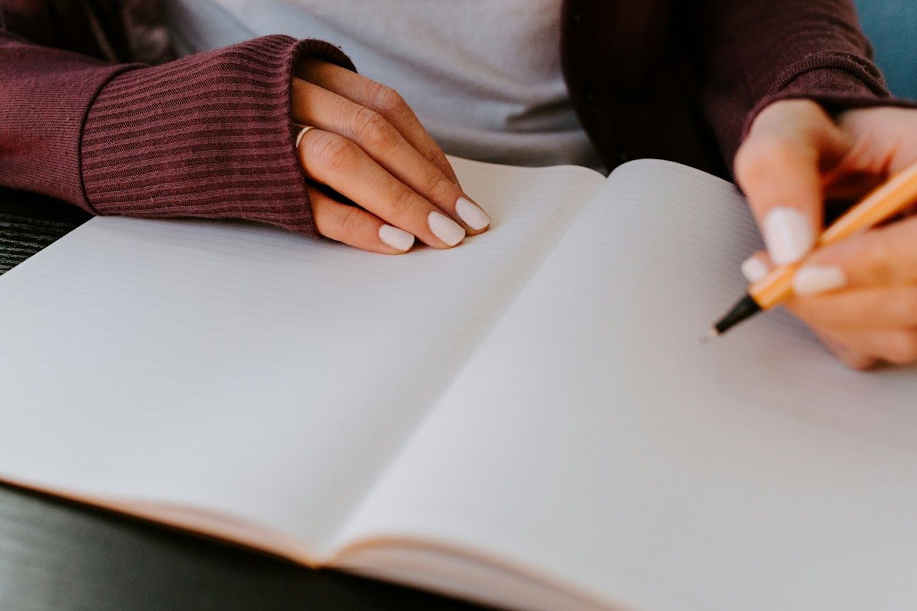 A woman is writing in a notebook with a pencil.