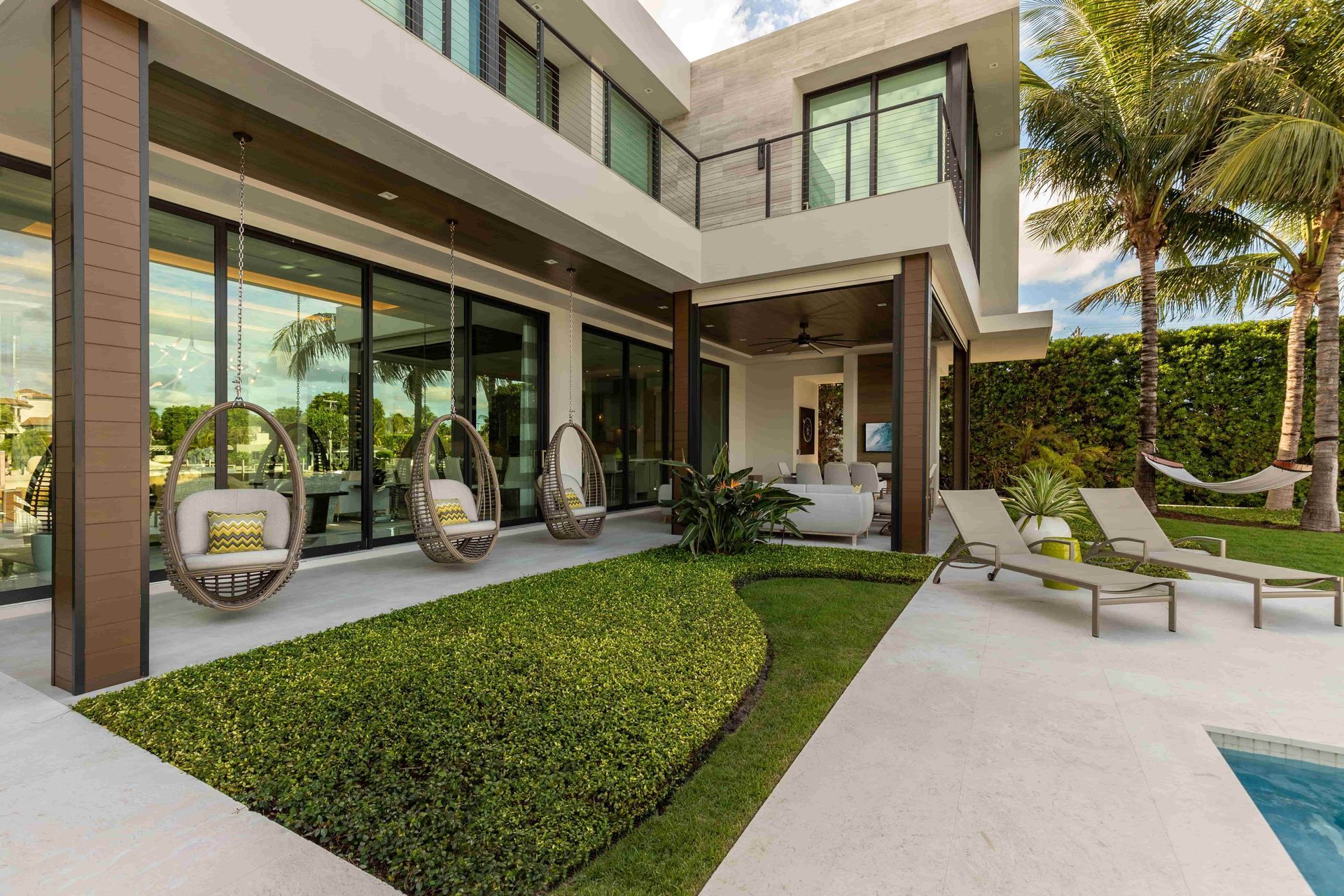 Modern home exterior with patio, hanging chairs, lawn, and pool.