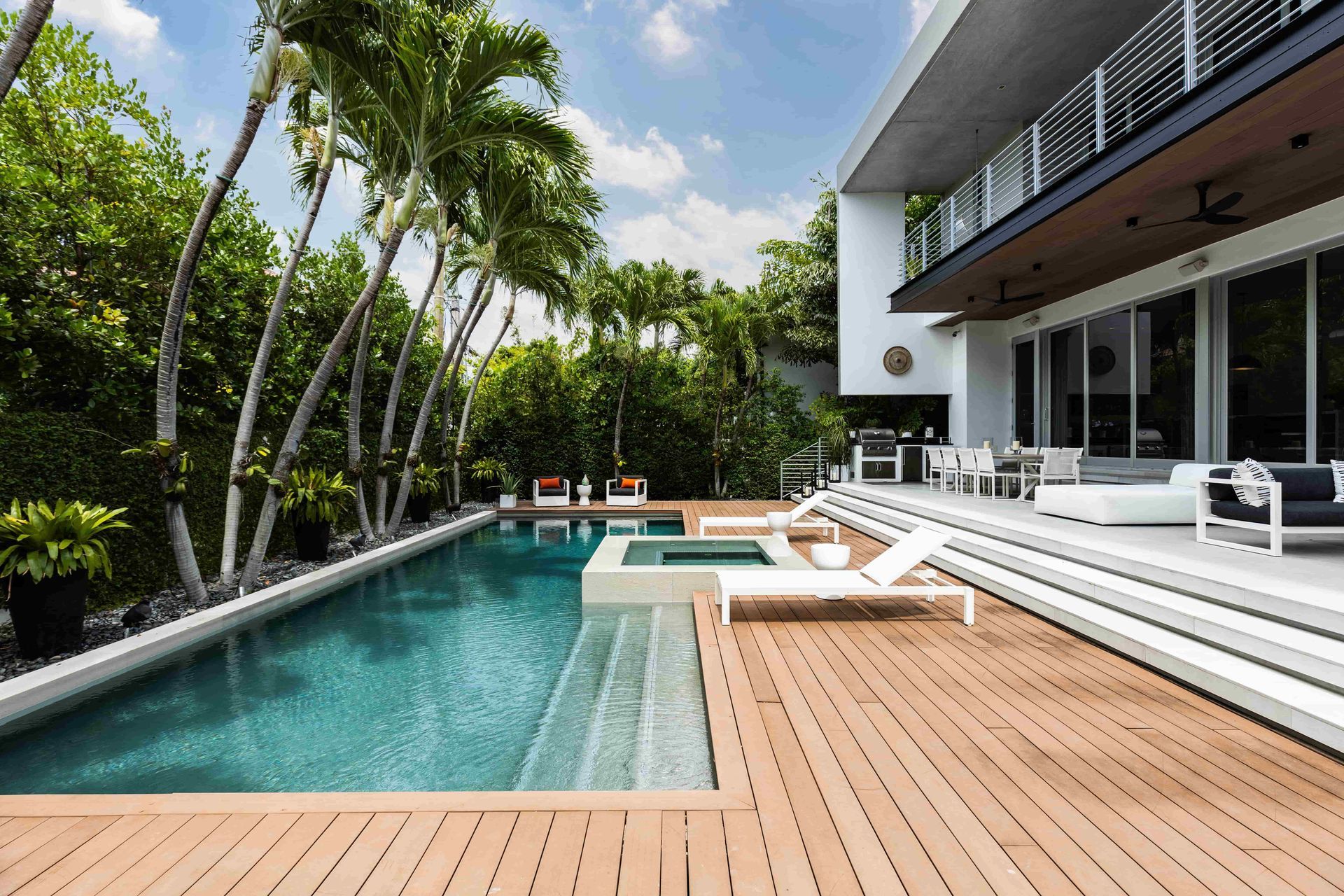 Modern home with pool, wooden deck, and lush tropical landscaping.