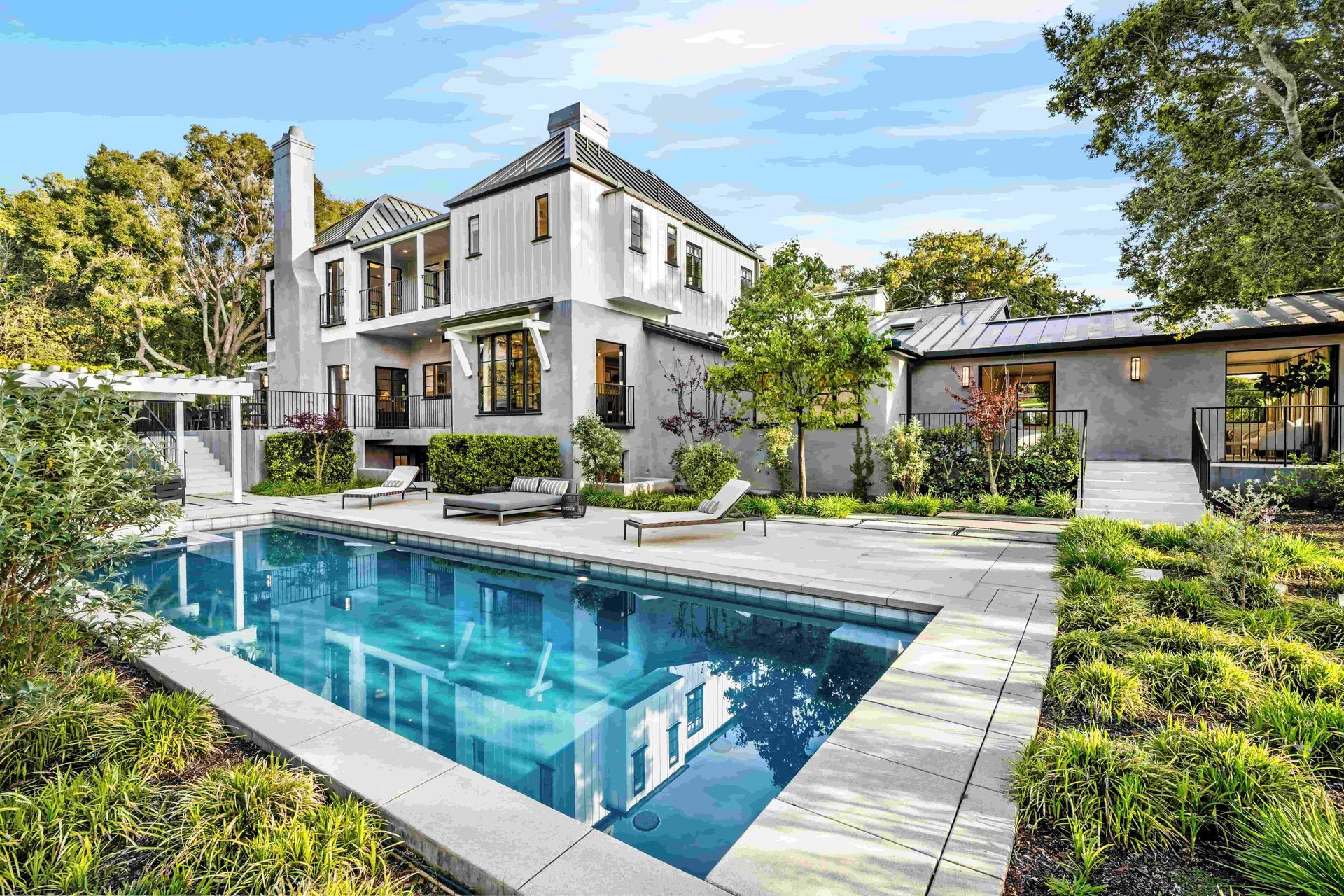 Luxury home exterior with pool, trees, and lounge chairs.