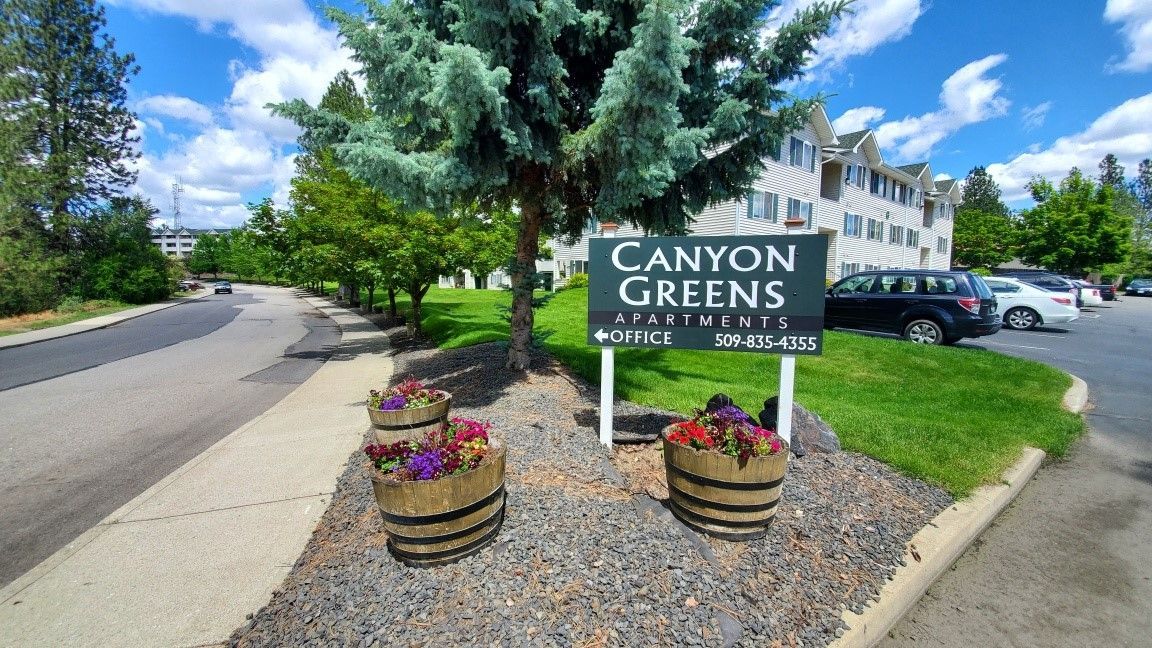 A sign for canyon greens is sitting in front of a building.