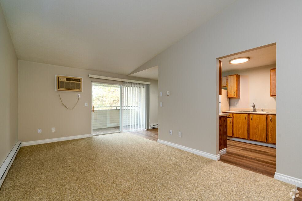 An empty living room with a sliding glass door leading to a kitchen.