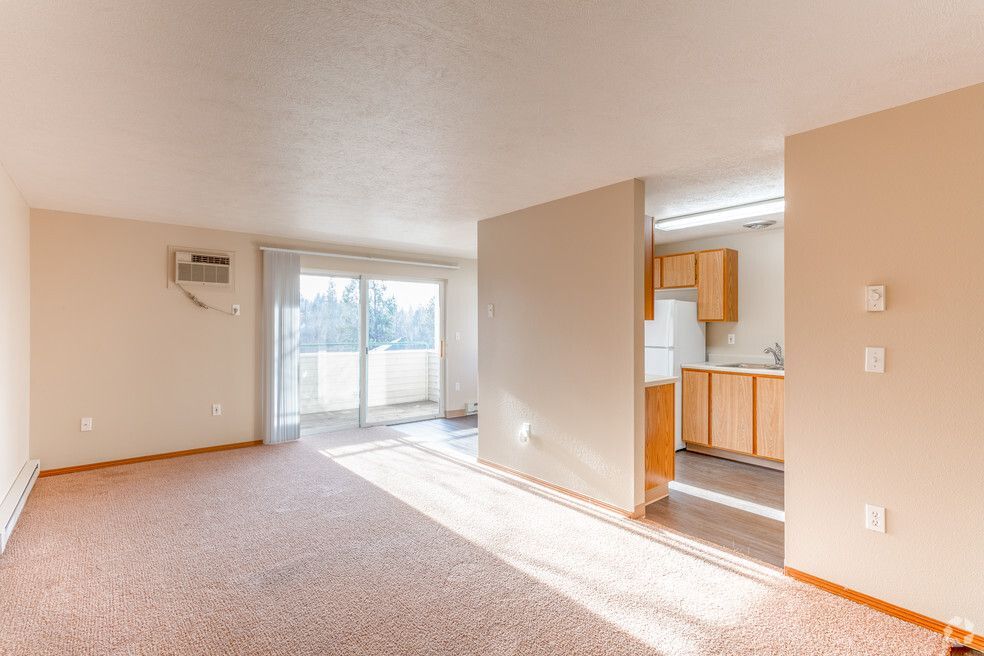 An empty living room with a sliding glass door leading to a kitchen.