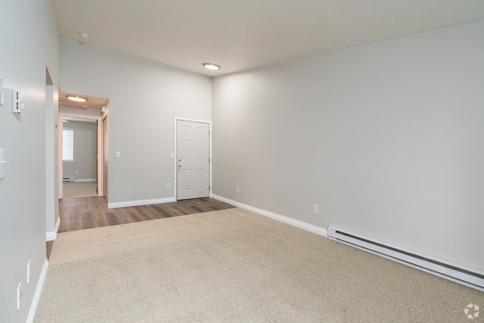 An empty living room with a carpeted floor and white walls.