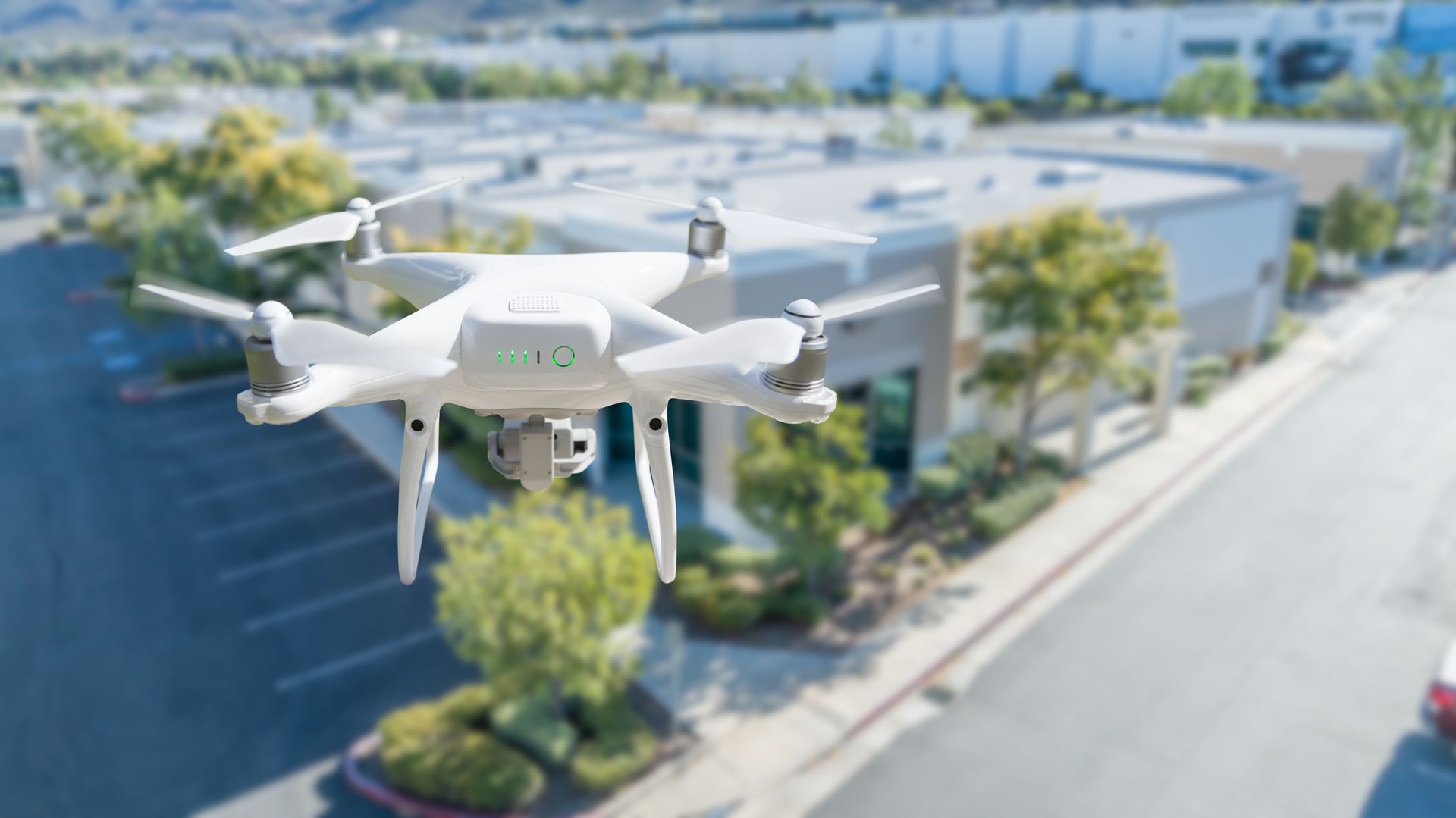 A white drone hovers in mid-air above a paved parking lot in front of a commercial building — Environment Restoration Solutions in Tweed Heads, NSW