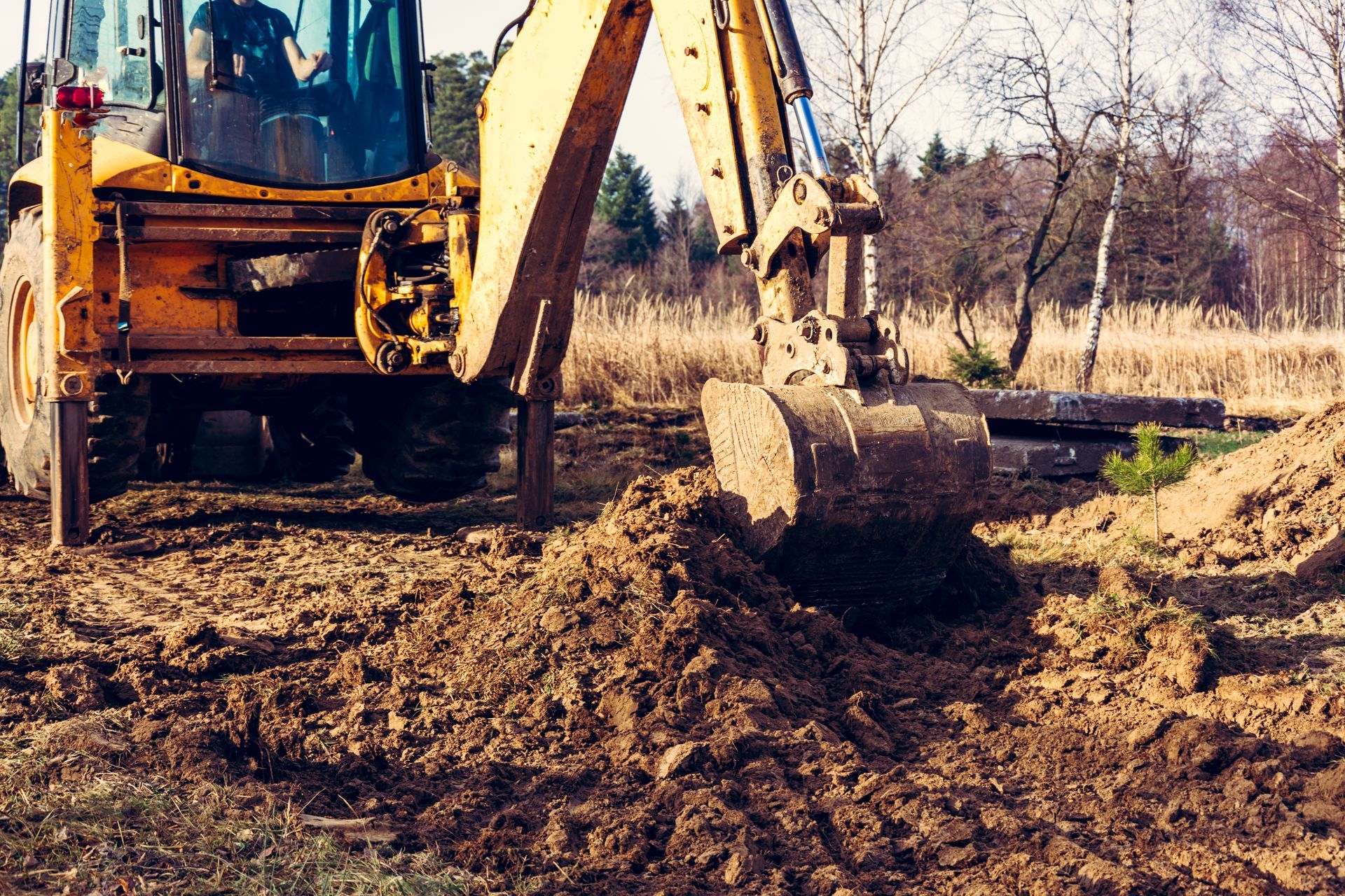 Yellow Backhoe Excavator Digs Into the Earth at an Outdoor Construction — Environment Restoration Solutions in Armidale, NSW