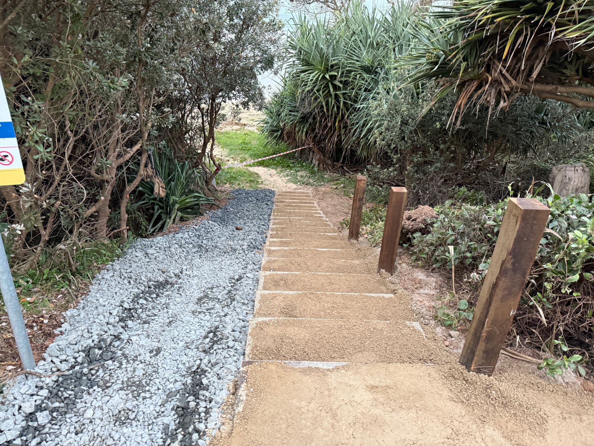 Narrow gravel and brick garden path bordered by shrubs and wooden posts in a wooded area