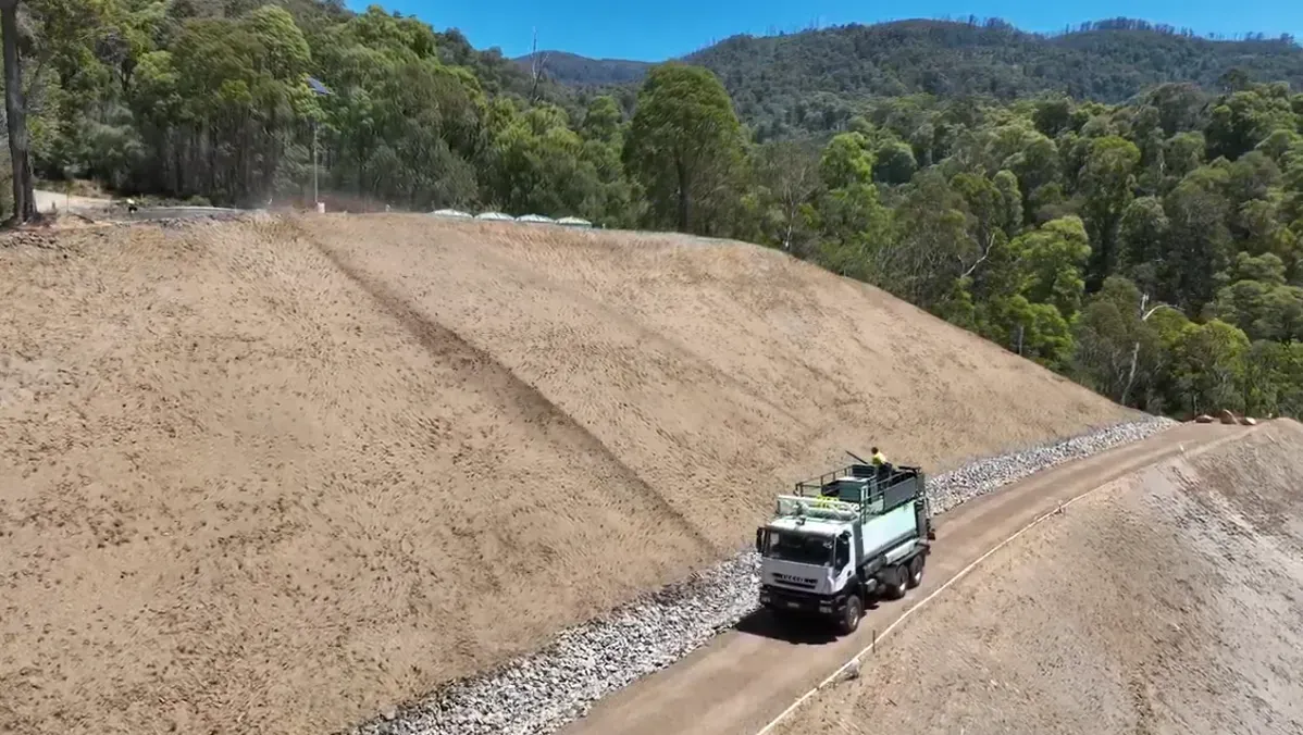 A white dump truck drives along a dirt road at the base of a large, cleared earth embankment — Environment Restoration Solutions in Waterview Heights, NSW