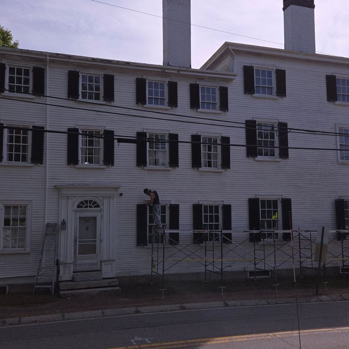 White building with black shutters; worker on scaffolding.