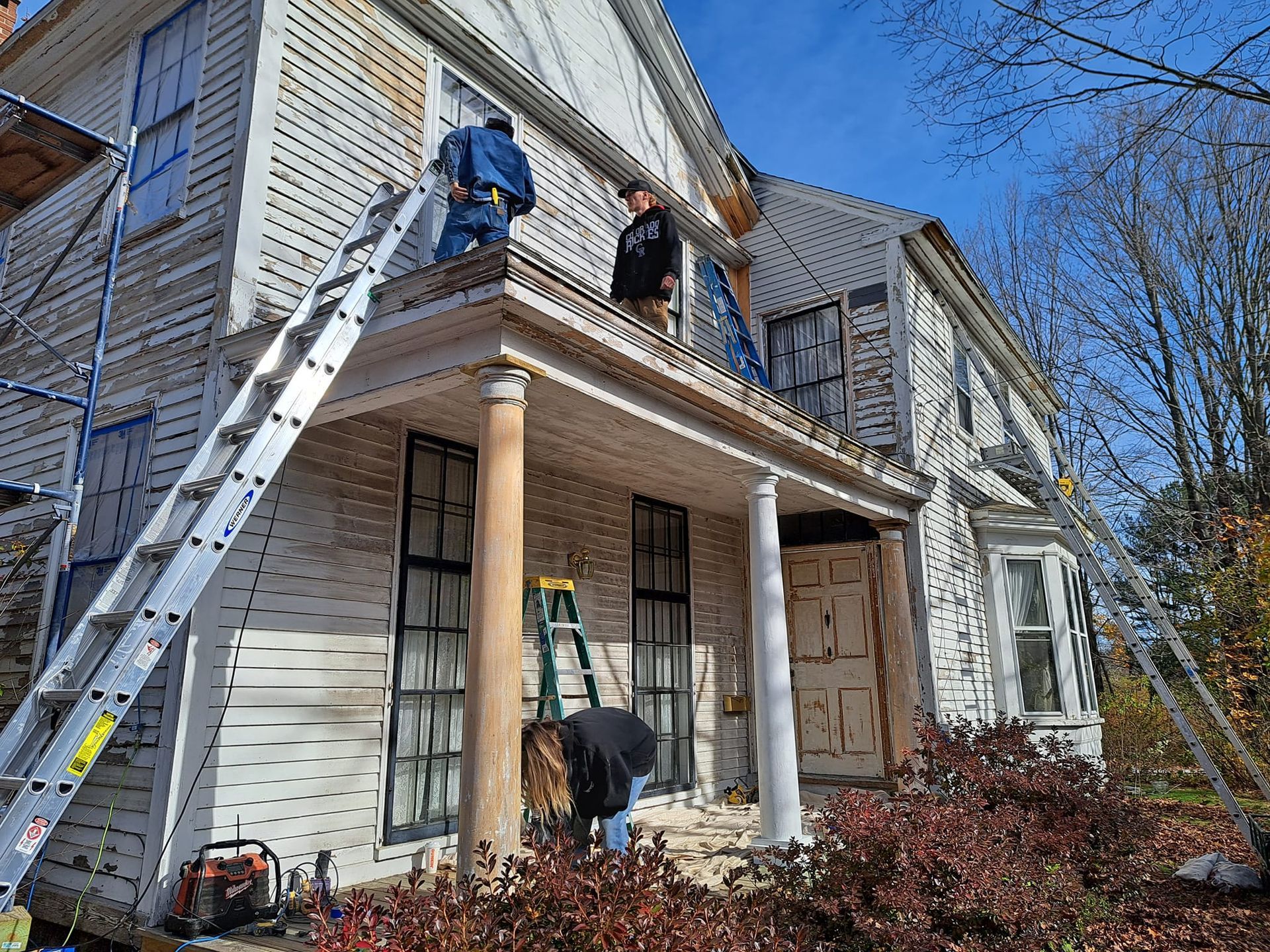 Exterior of a house being painted by workers on ladders. Porch has columns.