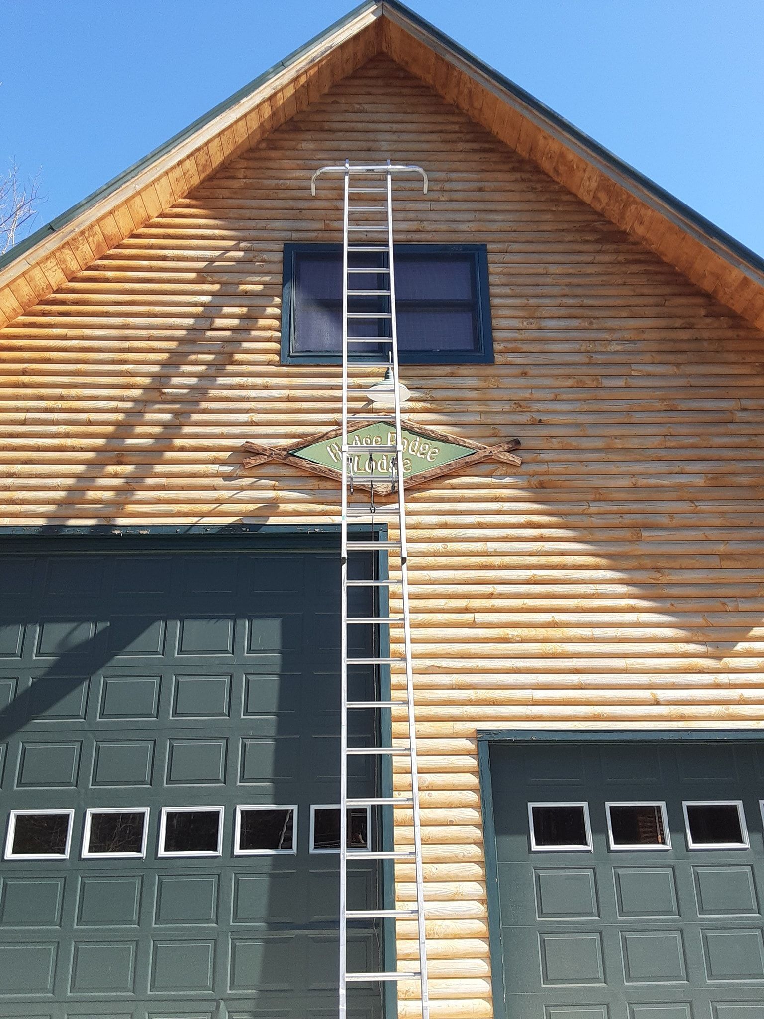Silver fixed ladder extends from garage roof to wooden building's peak.