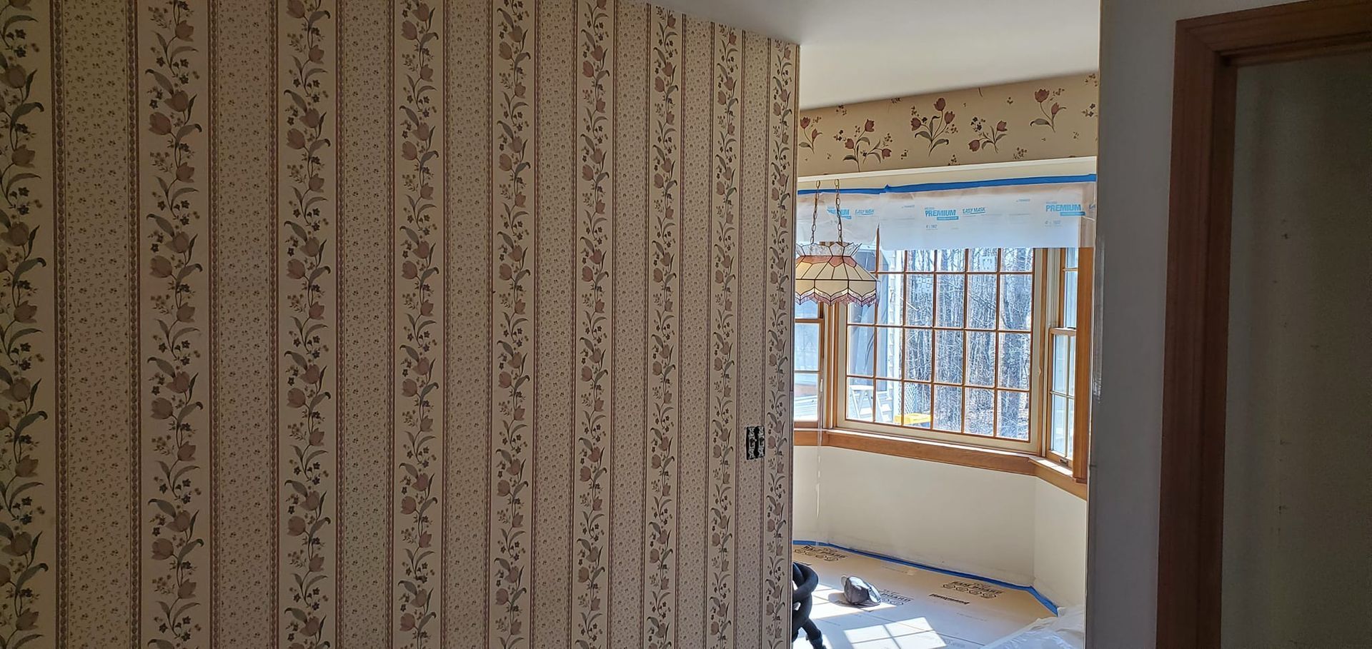 A hallway with floral wallpaper leads to a room with a bay window.