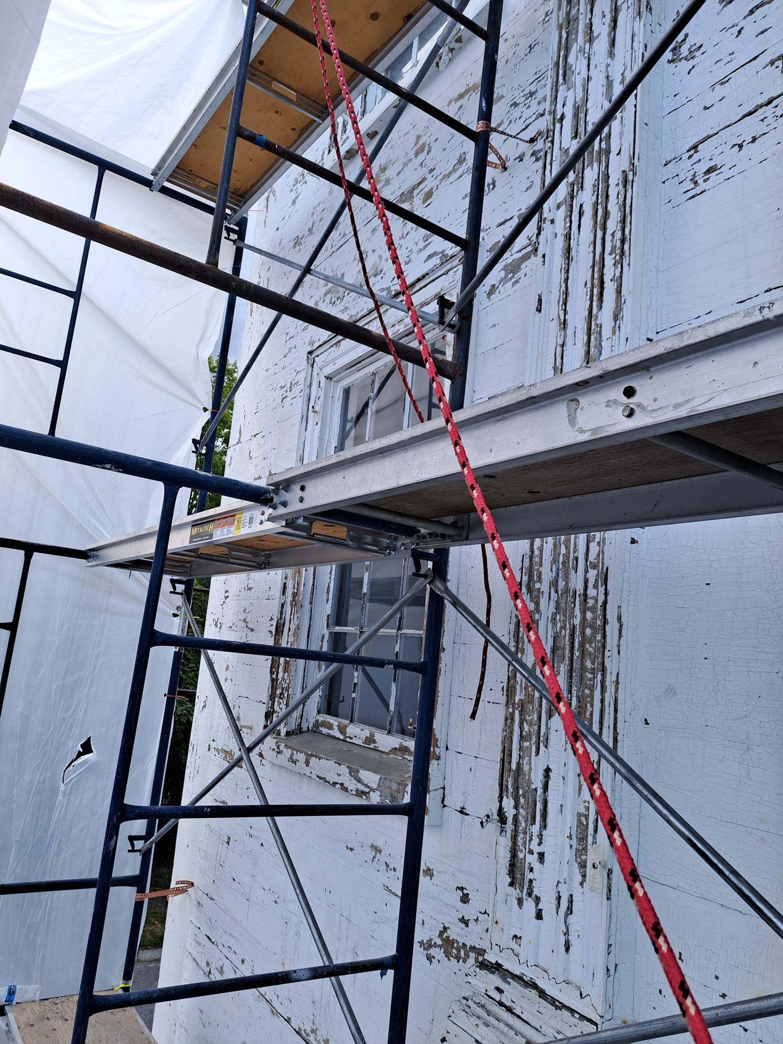 Scaffolding against a building with peeling paint; a red rope hangs down.