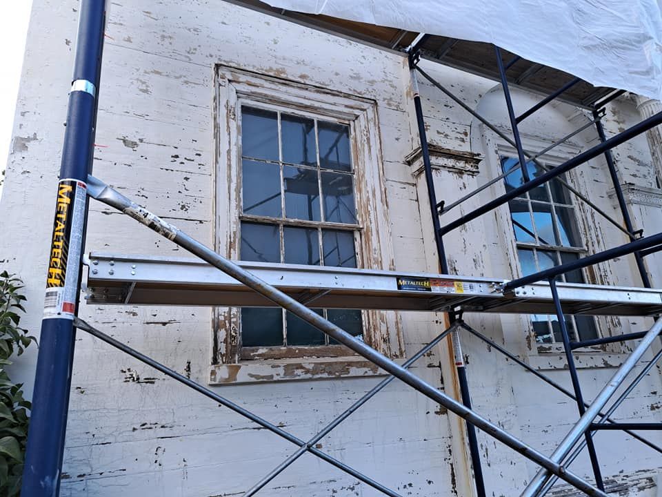 Exterior view of a building with scaffolding, windows, and peeling white paint.