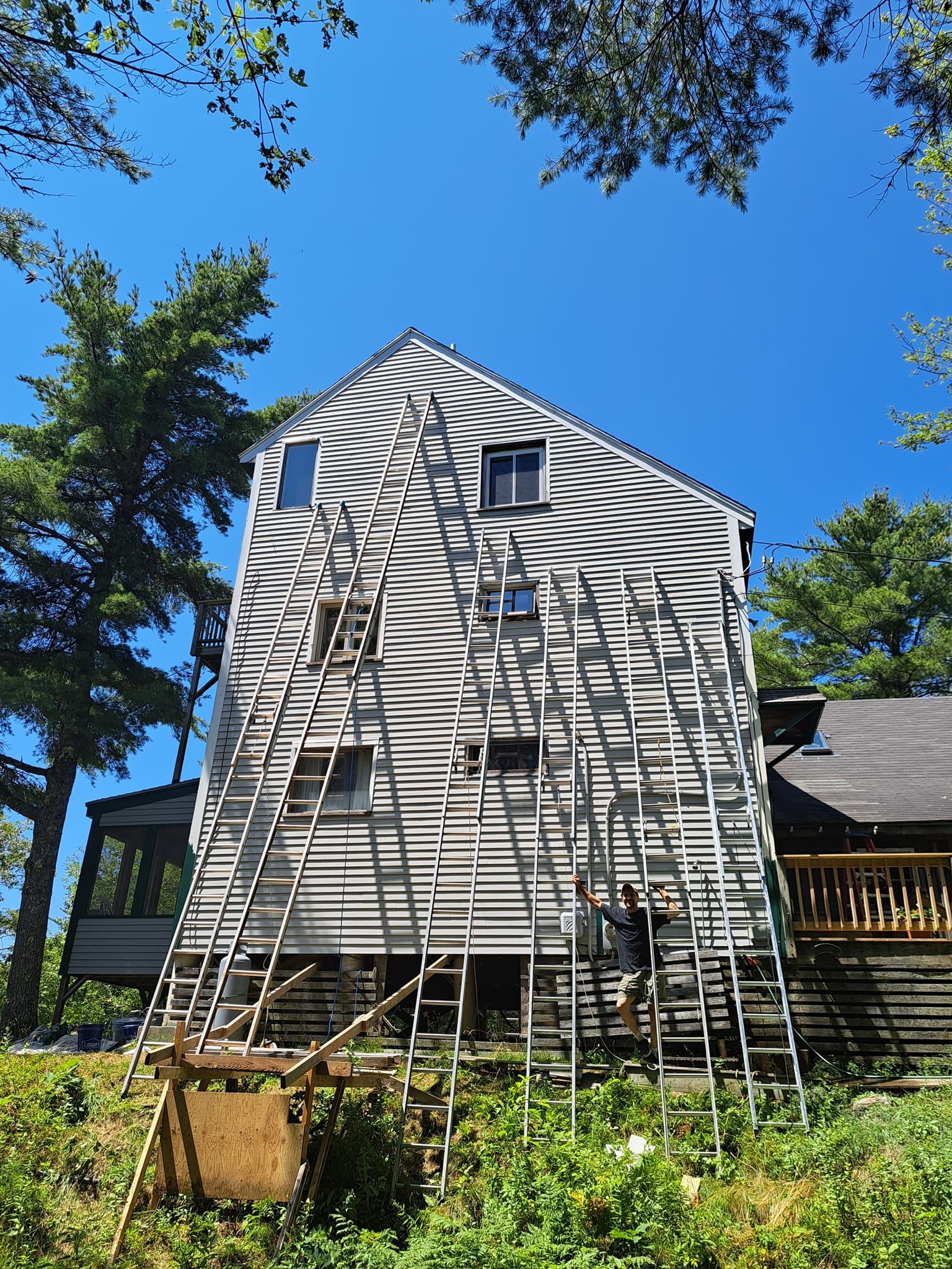 House with many ladders leaning against it, sunlight creating striped shadows.
