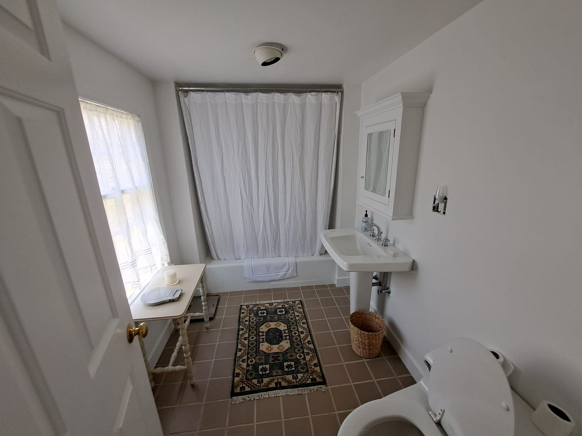 Bathroom interior with a shower, toilet, sink, rug, and window.