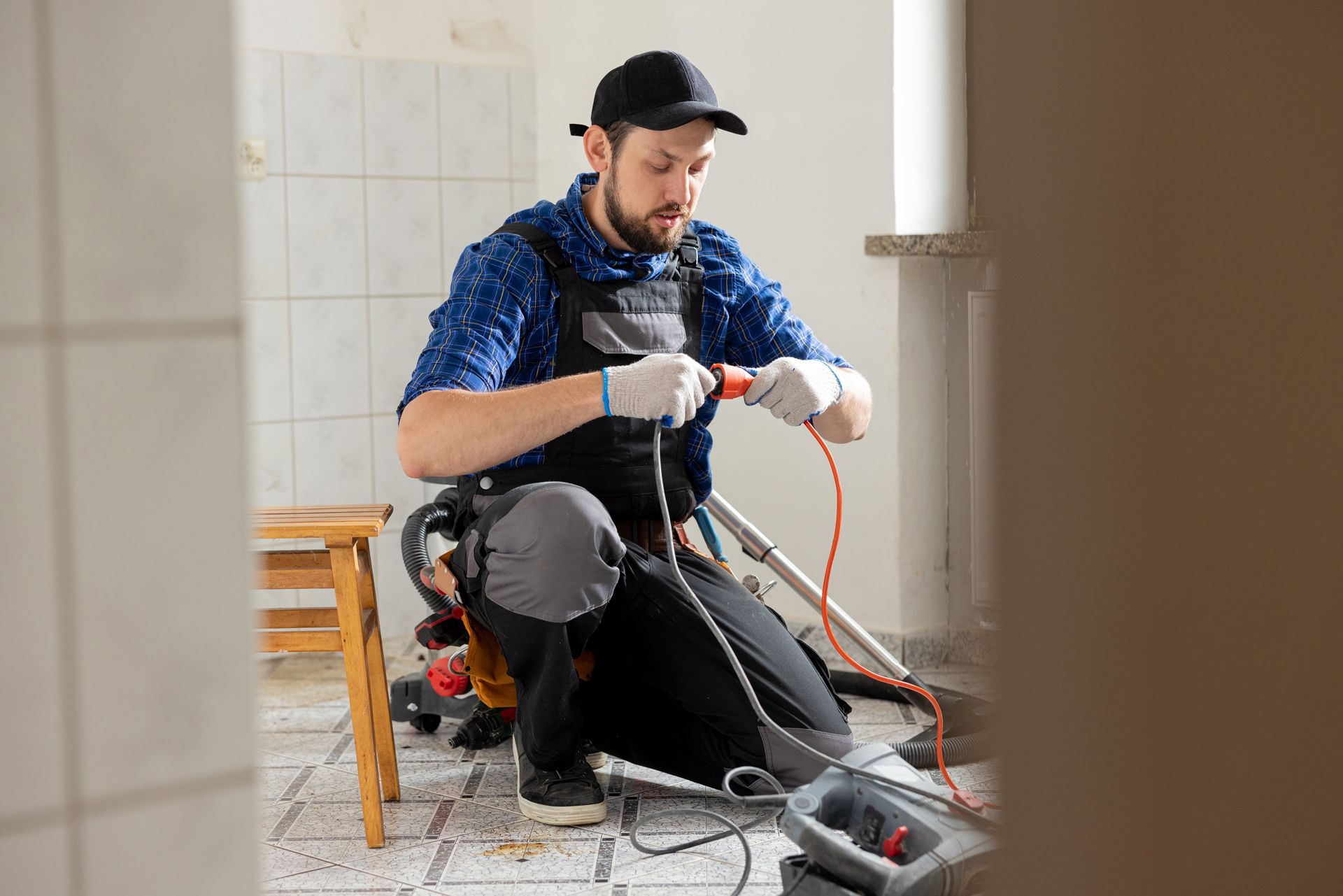 Plumber kneeling, working with wires in a room under construction.