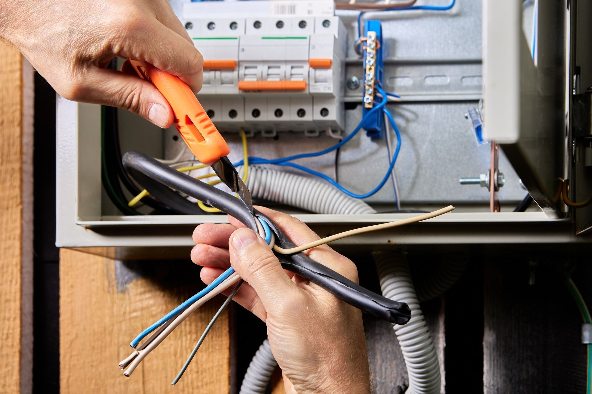 Hands working on electrical wiring in an open fuse box, using a knife.