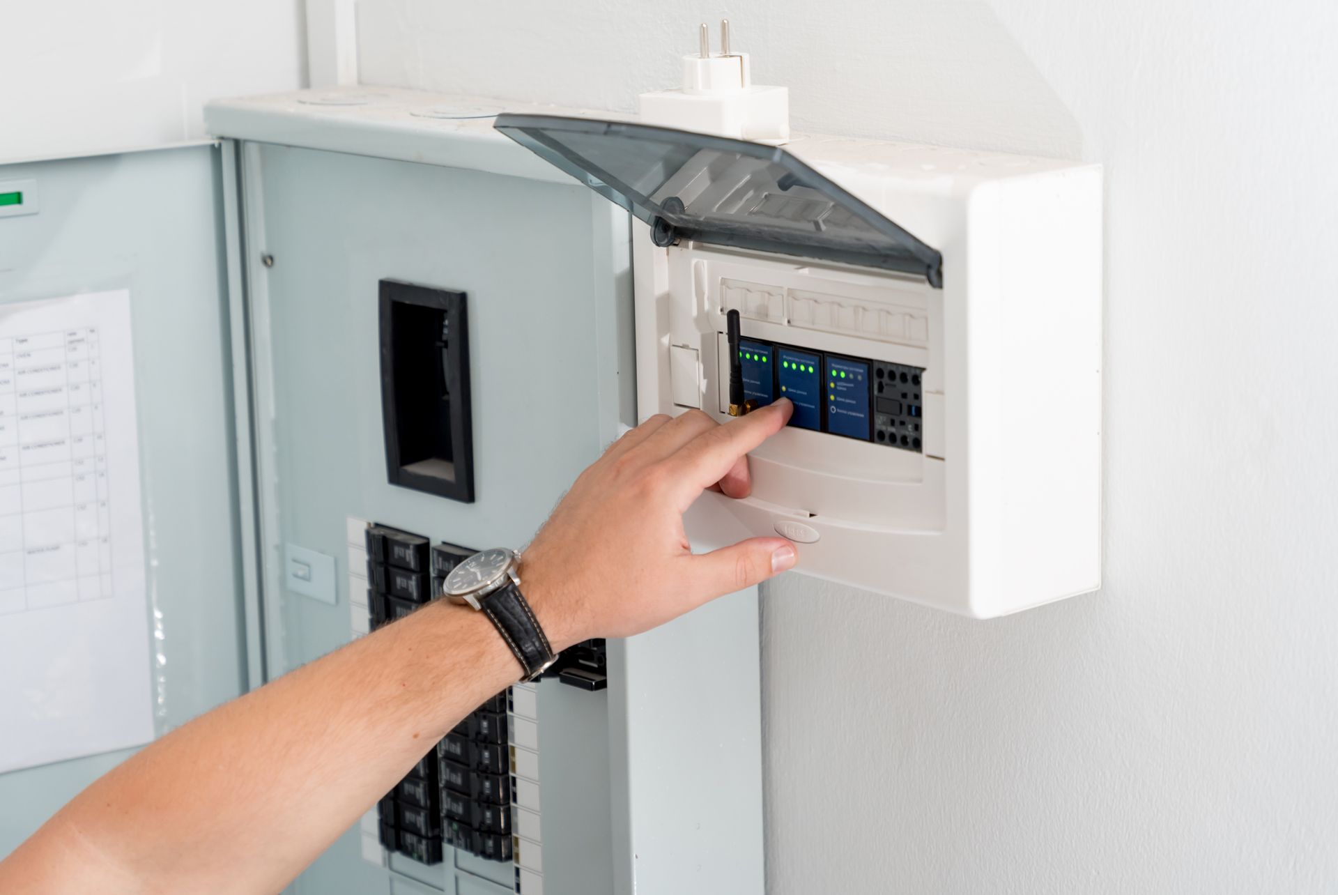 Hand reaching towards a circuit breaker panel, likely resetting a switch.