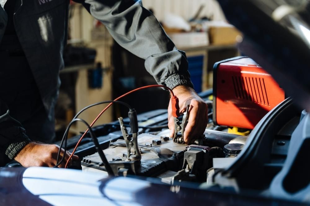 A Man Is Charging a Car Battery with A Charger — Belmont Auto Electrics in Belmont, NSW