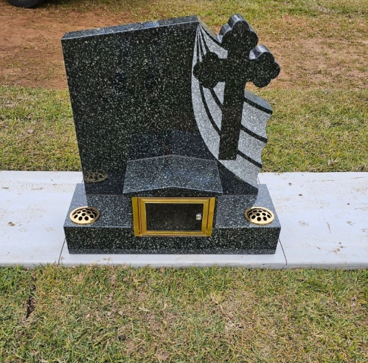 Black granite tombstone with a cross carving, a small window, and two flower holders.