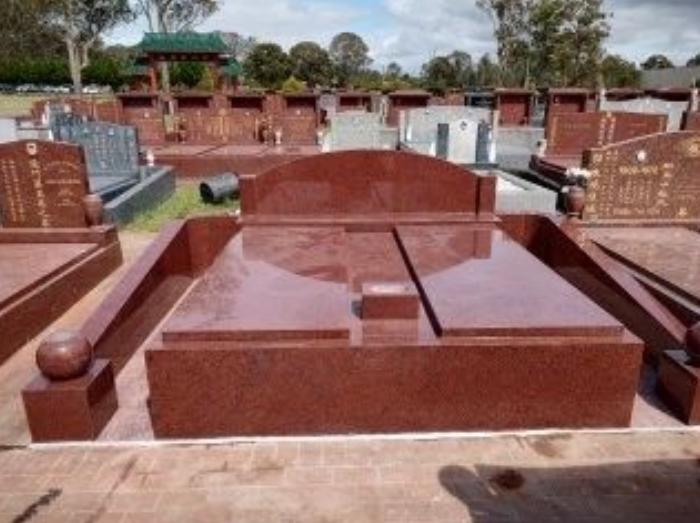 Red granite tombstone in a cemetery, with a flat central section and arched head.