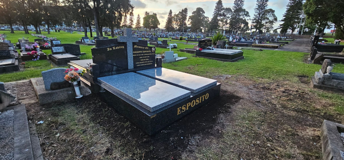 Cemetery with numerous gravestones and a large, newly placed black headstone in focus.