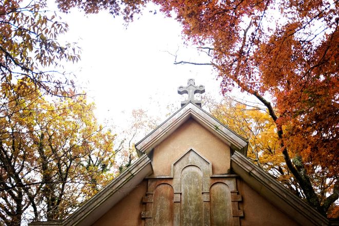 Gabled tomb with a cross, framed by autumn trees with orange and yellow leaves.