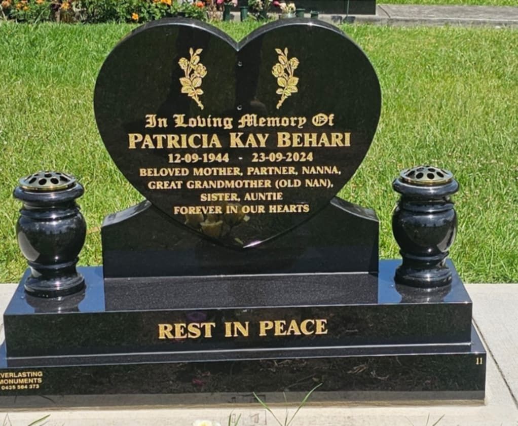 Black heart-shaped headstone with engraved text and flower vases. 