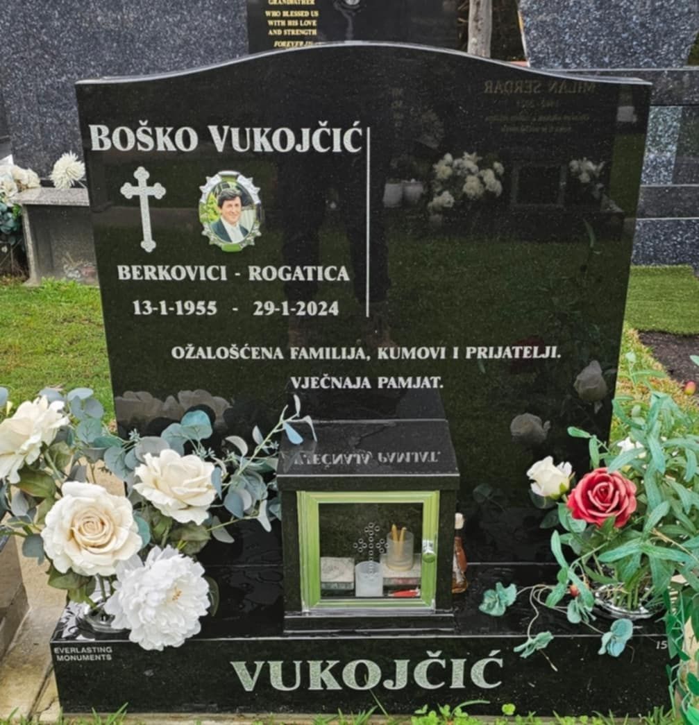 Black tombstone with name, birth/death dates, photo, and inscription. Flowers and a lantern are in front.