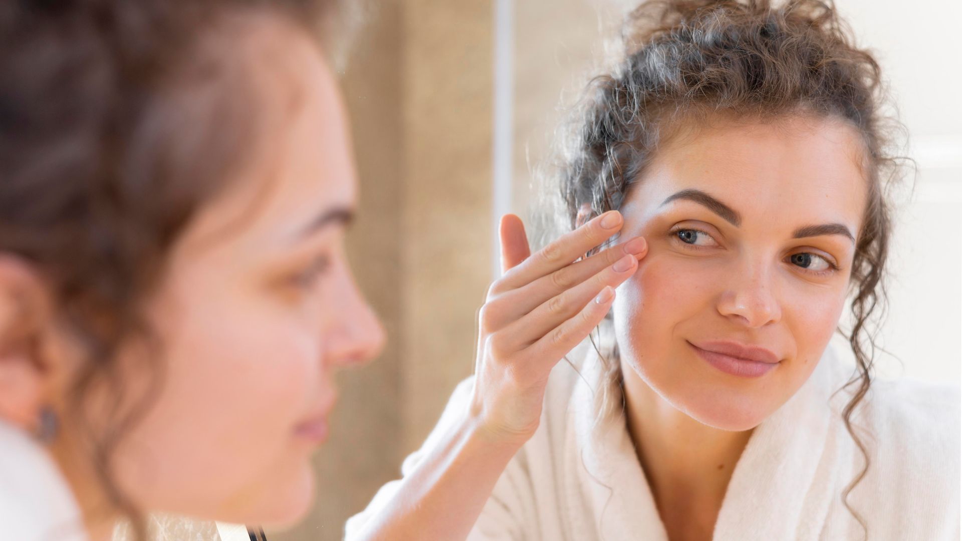 A woman is looking at her face in the mirror.
