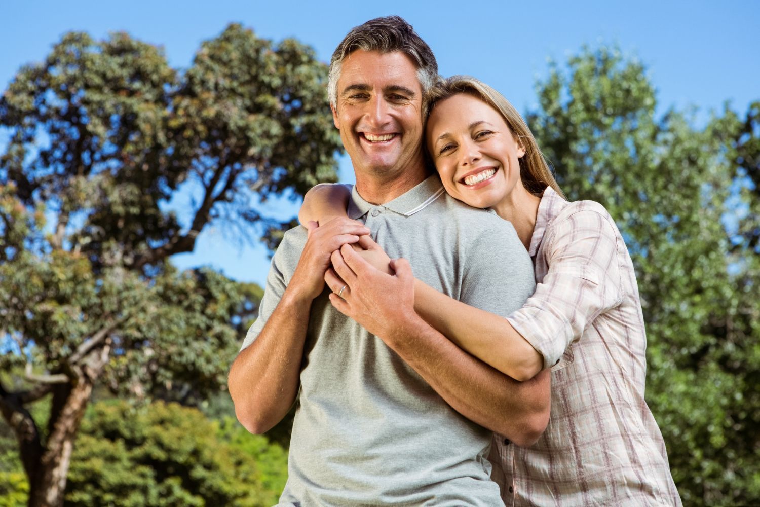 Smiling couple embracing outdoors with trees and blue sky in the background