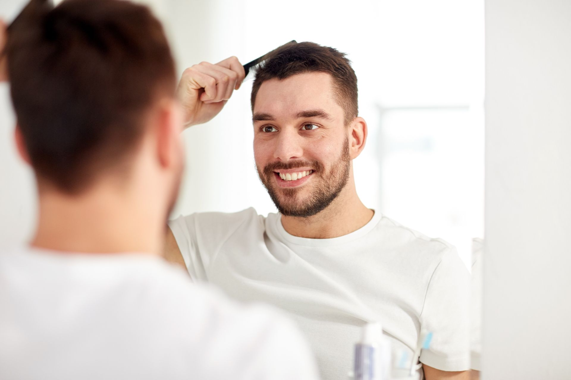 A man is brushing his hair in front of a mirror.