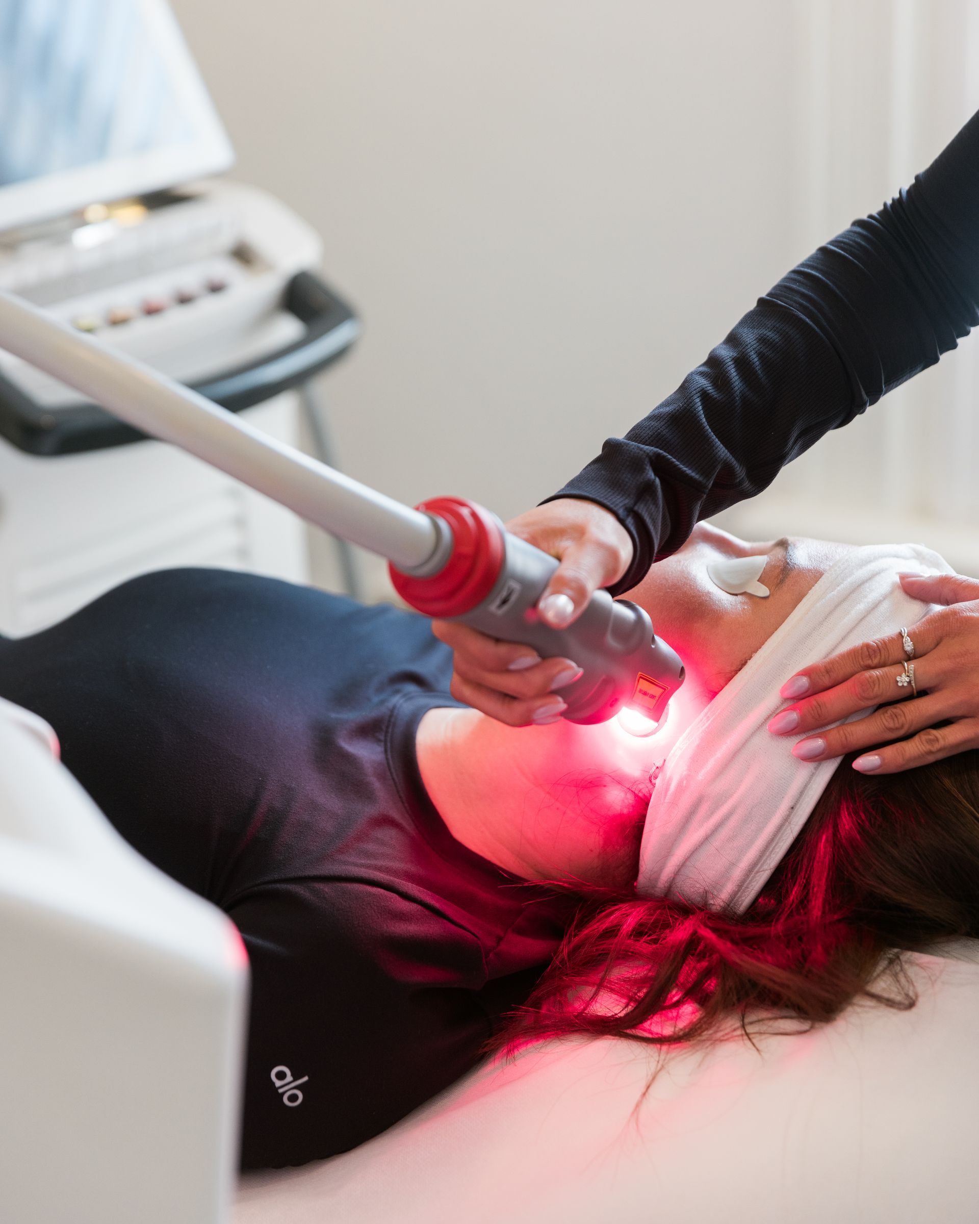 A woman in a white coat is touching her face with her hand.