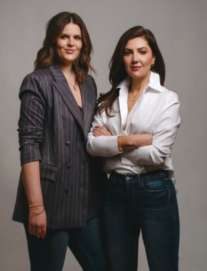 two women are standing next to each other with their arms crossed .