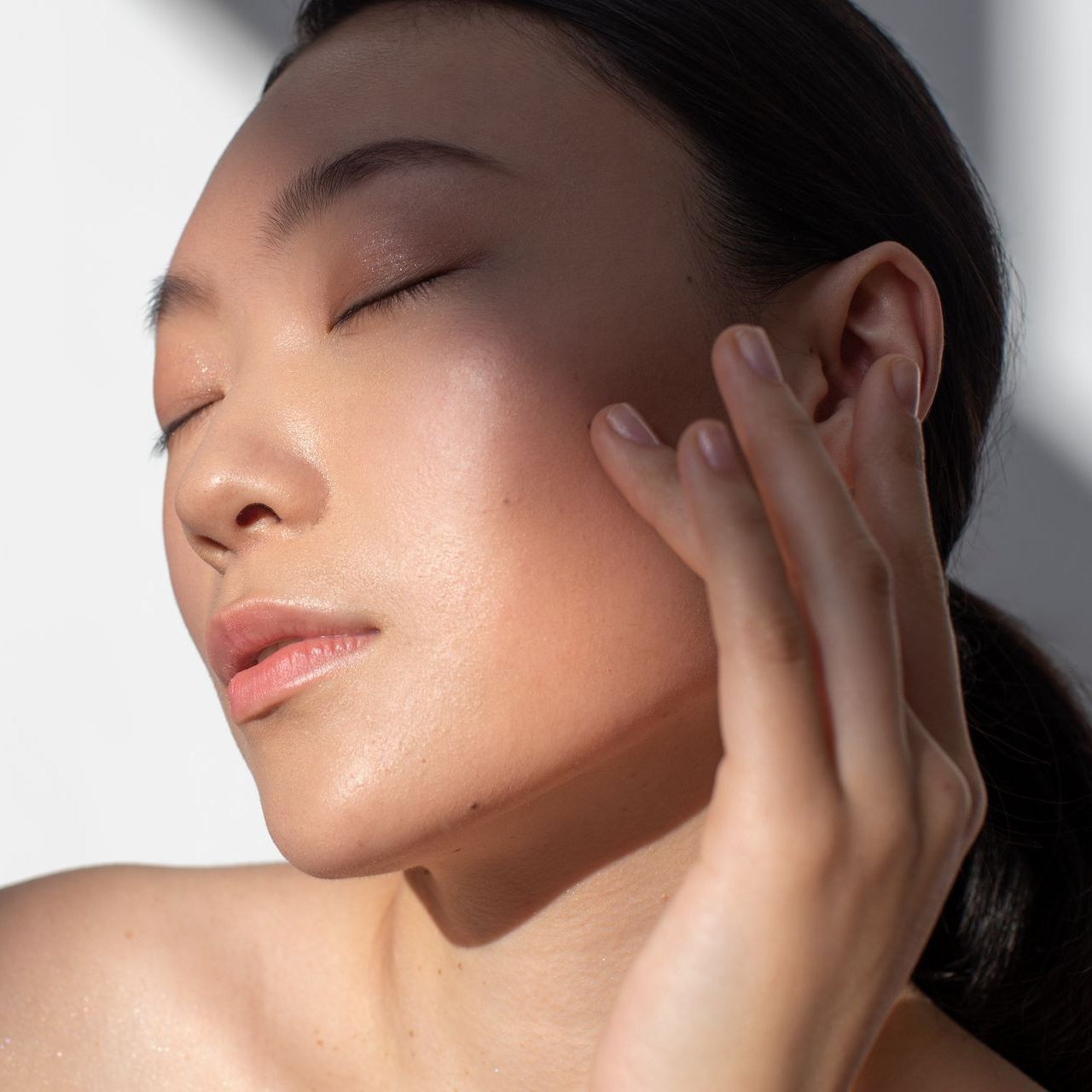 A close up of a woman 's face with her eyes closed and her hand on her face.