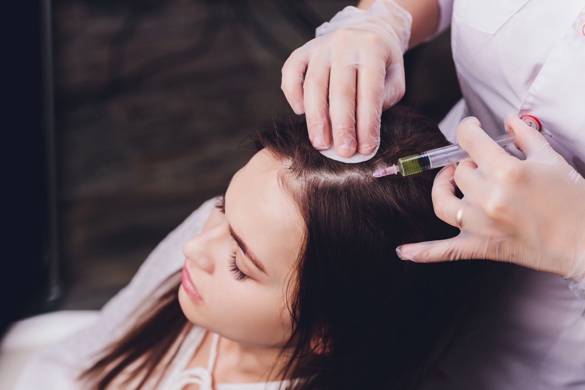 Woman receiving scalp injections from a gloved medical professional.