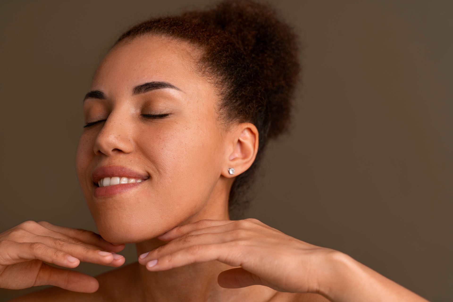 A woman is smiling and touching her face with her hands.