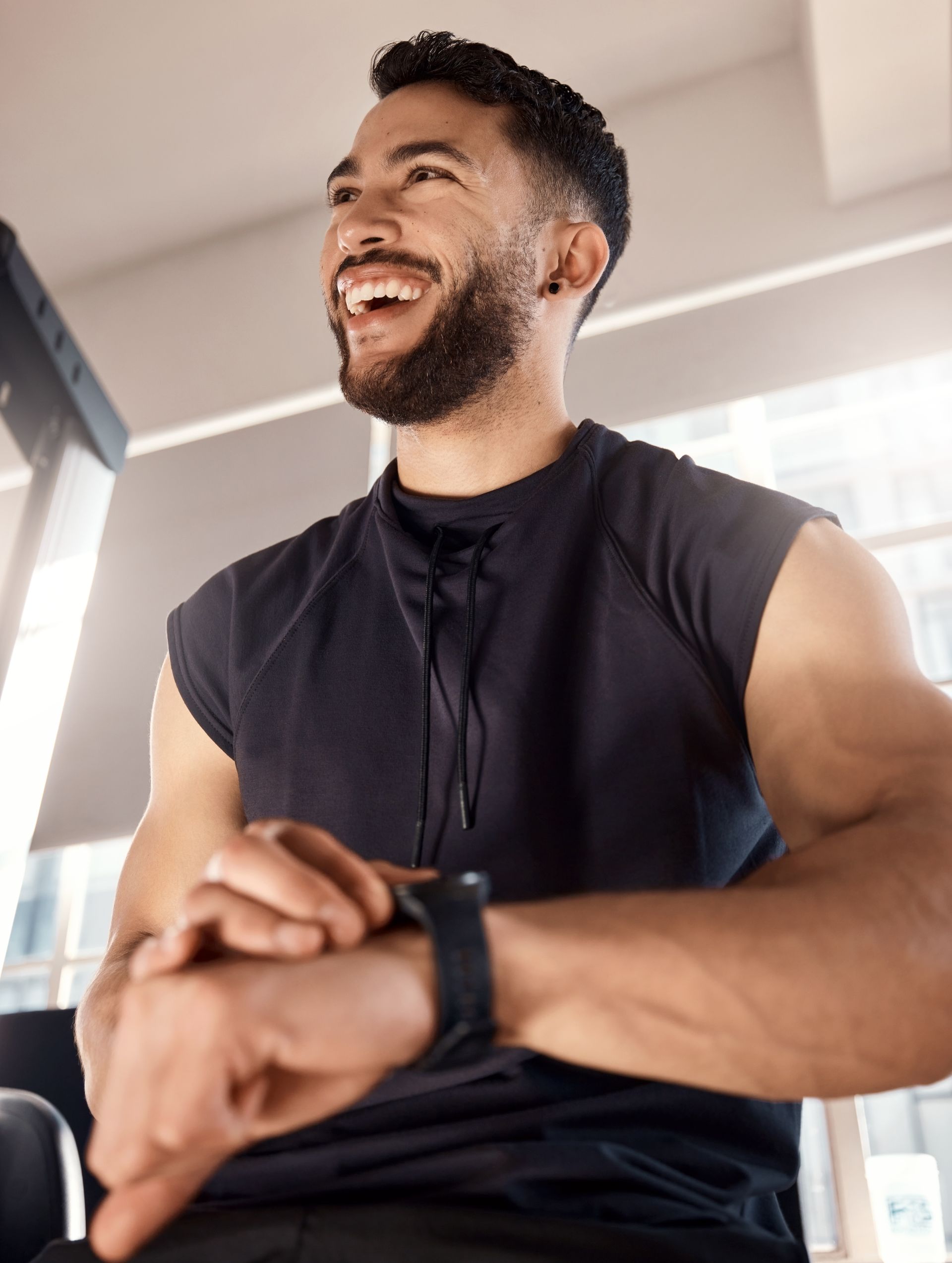 A man is laughing while looking at his watch in a gym.