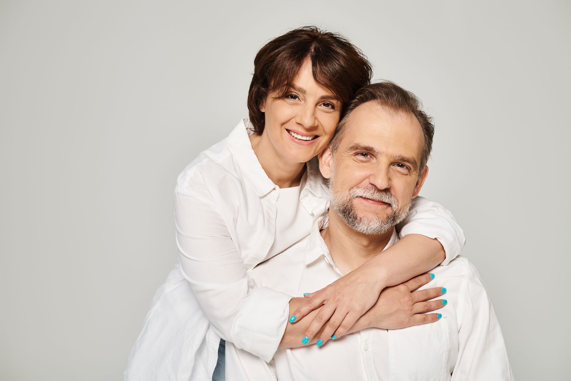 A woman is hugging a man from behind on a gray background.