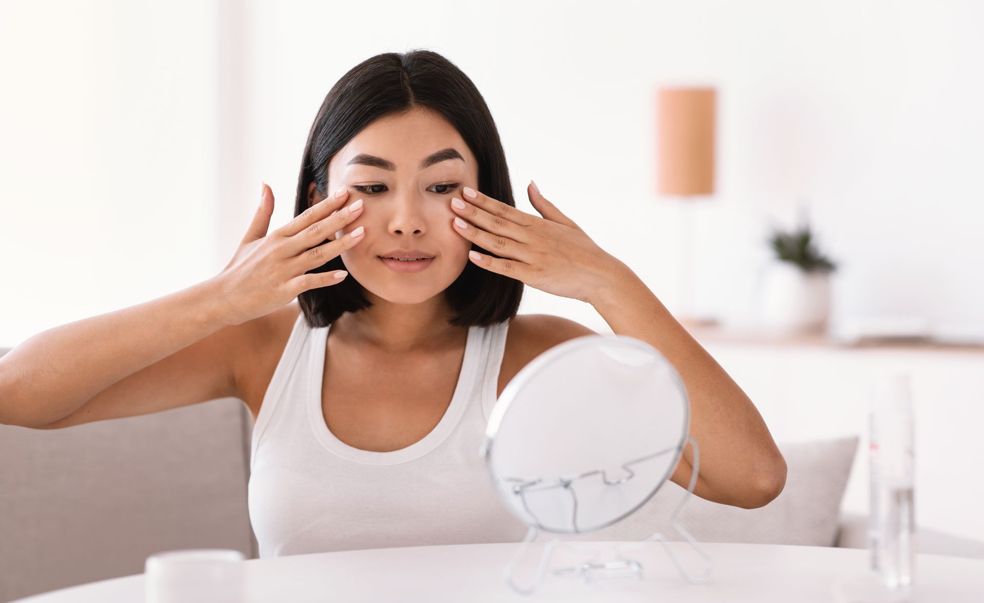 A woman is looking at her face in a mirror.