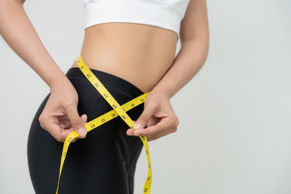 A woman is measuring her waist with a yellow tape measure.