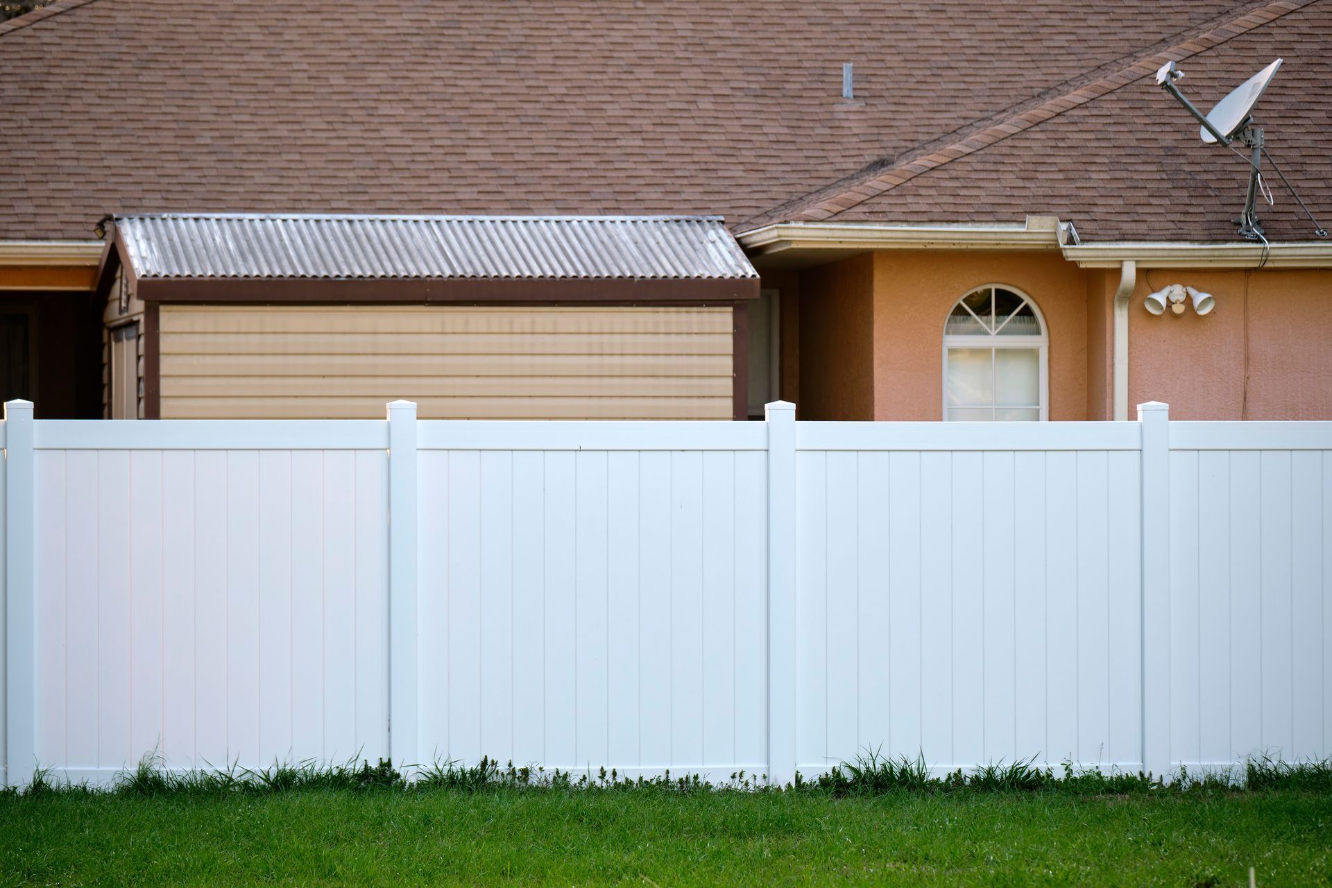 White vinyl privacy fence enclosing a backyard with a house and storage shed behind it.