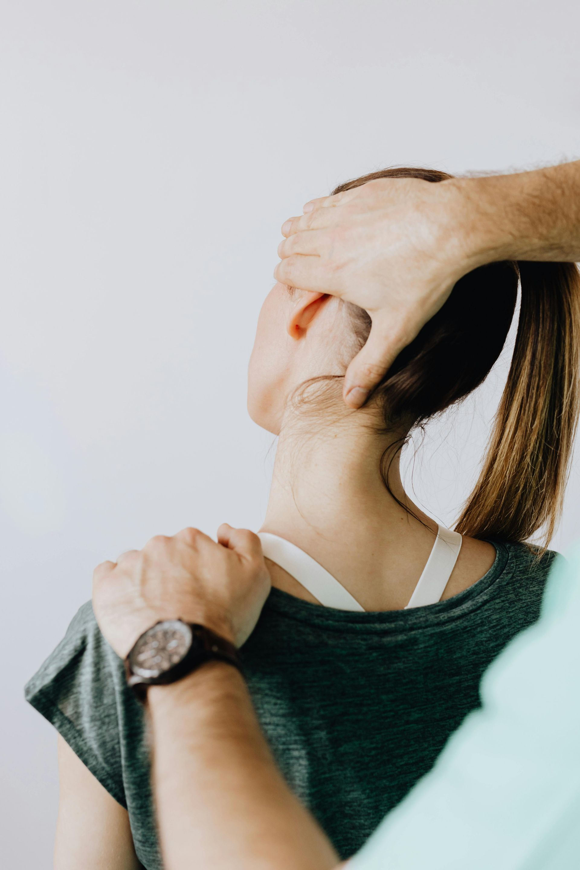 Person receiving a neck adjustment from another person. White setting. Hands on head and shoulder.