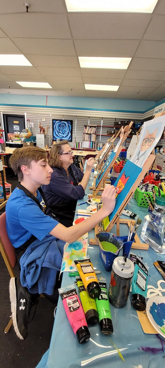 A group of people are sitting at a table painting.