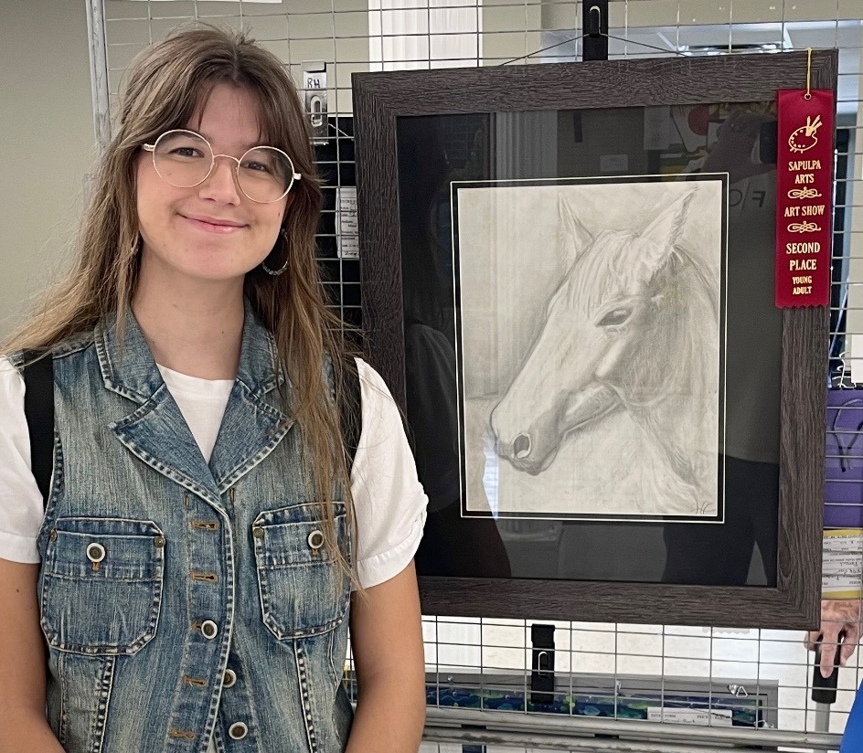 A young woman is standing in front of a framed drawing of a horse.