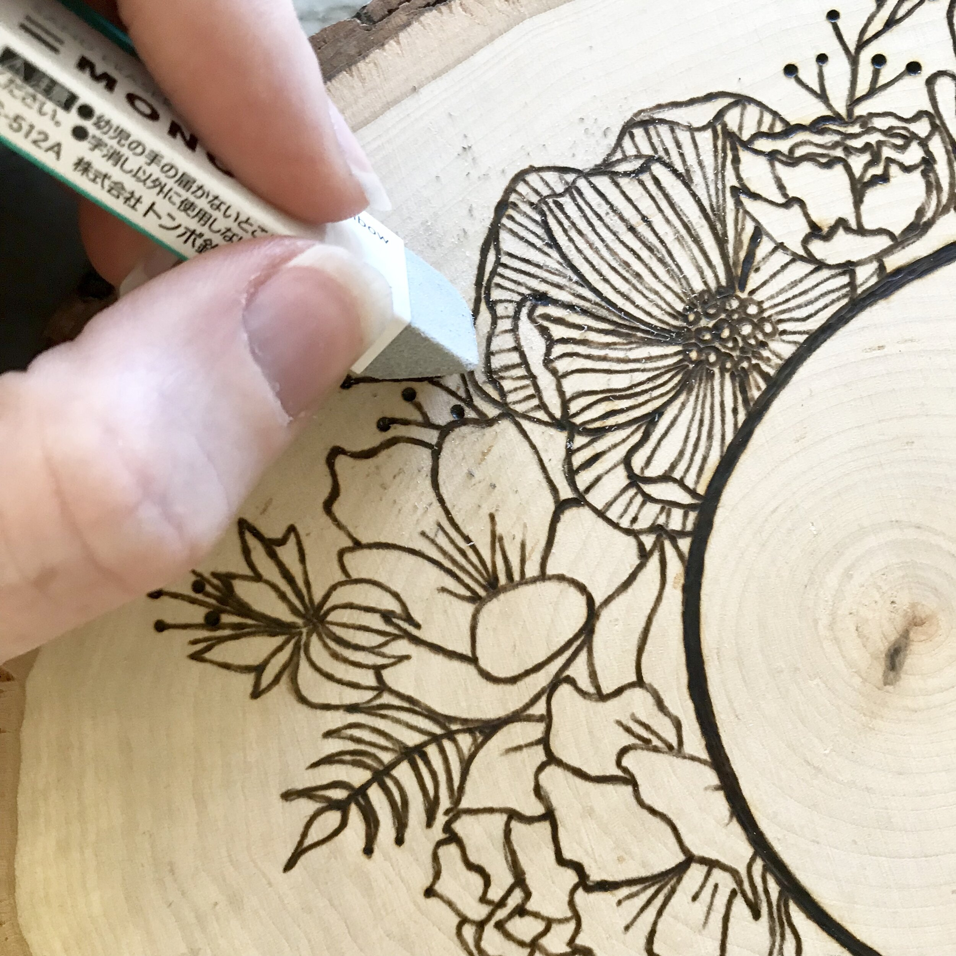 A person is erasing a drawing of flowers on a piece of wood